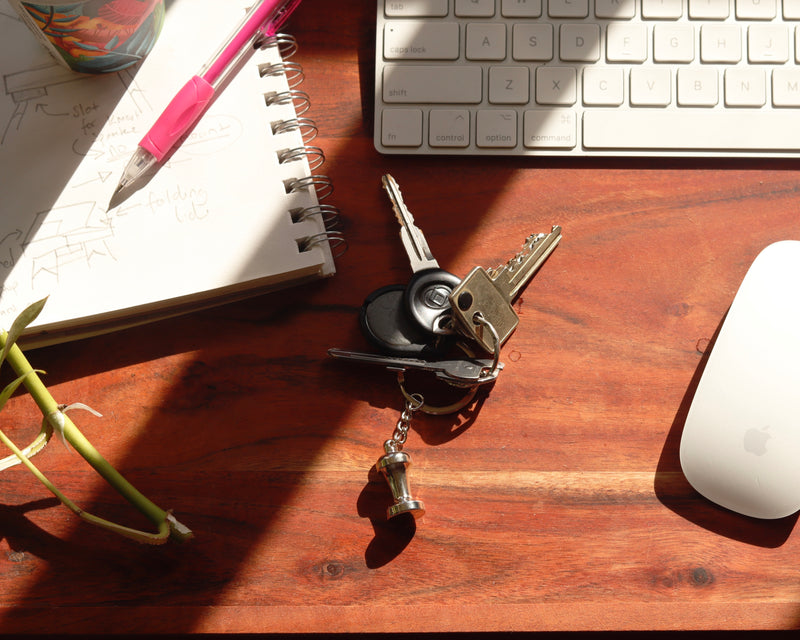 Rosso Tamper keychain charm on desk with coffee and keyboard