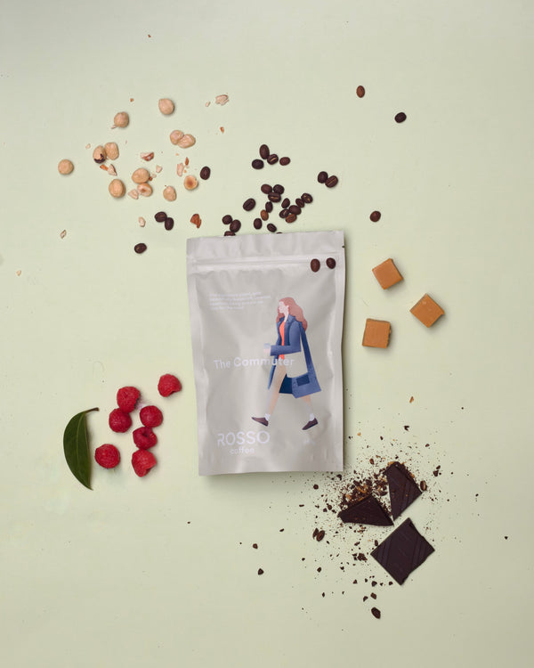 A Bag of Rosso Coffee the Commuter blend on a pastel background surrounded by nuts, berries and chocolate.